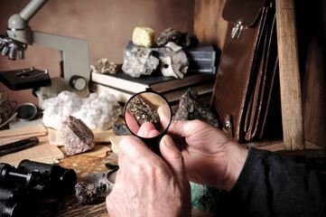 Geologist examining a mineral sample under a magnifying glass - obrazy, fototapety, plakaty