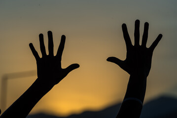 person making silhouettes with their hands in the darkness of a sunset