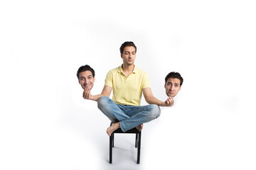 Young man sitting in lotus pose and holding masks with different mood isolated on white