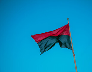 Fototapeta Red-black flag of Ukrainian nationalists, isolated on a blue sky background, close-up. Background of silk fabric fluttering in the air. obraz