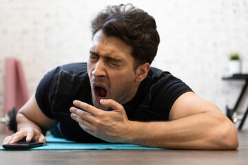Tired young man yawning while training on the floor at home. Do sport and exercise at the morning...