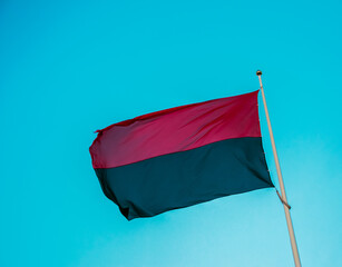 Fototapeta Red-black flag of Ukrainian nationalists, isolated on a blue sky background, close-up. Background of silk fabric fluttering in the air. obraz