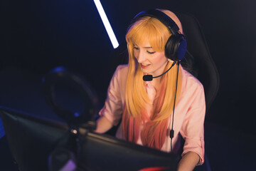 Young blonde gamer girl talking through headset with her teammates competing in online game...