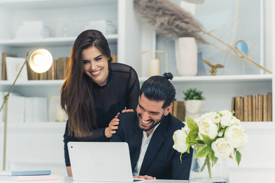 Girlfriend acting playfully with businessman boyfriend working from home sitting by desk in front of laptop. Laughing couple. Indoor shot. High quality photo