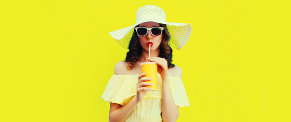 Portrait of beautiful young woman drinking fresh juice wearing white summer straw hat on yellow...