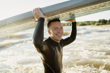 Portrait of a smiling man surfer in a wetsuit on the waves at sunset in the sea