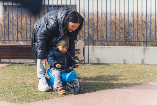 The young beautiful mother is taking care and teaching his small cute african child to ride a baby bike in a background area near the fence. High quality photo
