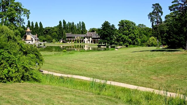 Versailles, Paris, France, June 2022. Nice pov footage walking towards the Hameau de la Reine in the Petit Trianon park. People walk the paths in the middle of the meadows. Beautiful summer day.