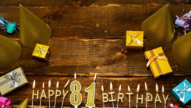 golden letters of the candle with the number happy birthday, the background of the gift boxes with candles happy birthday on the background of brown boards. Copy spacePostcard Happy birthday 81