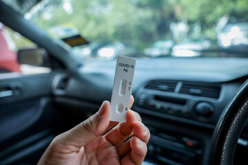Cropped hand holding a Covid19 test kit with car dashboard at the back