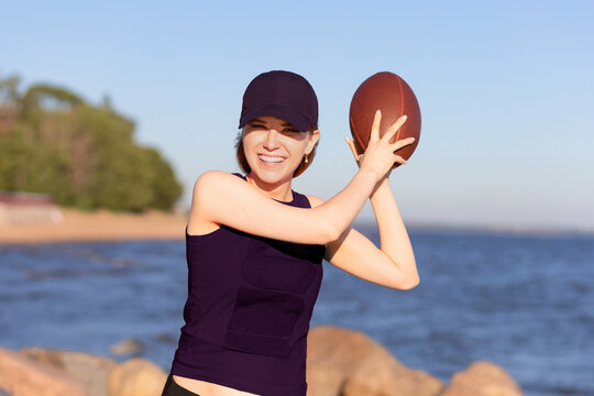 Happy European Girl Playing, Winning In American Football On Beach. Young Female Team Player With Rugby Ball Smiling, Laughing. Prefabricated Games, Pastime, Sports, Active Recreation For Youth