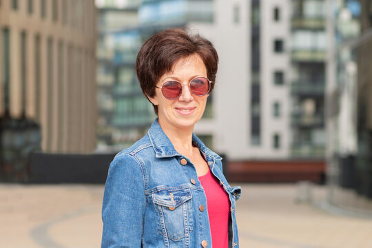 portrait positive smiling middle aged jewish woman in trendy modern sunglasses on sunny day. happy european adult lady in summer city. female Jew laughing near business center