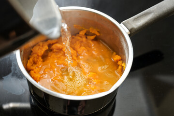 Pureed carrots are poured with boiling water in a steel pot, cooking a healthy digestible vegetable...