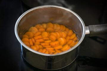 Slices of carrot are cooked in water in a steel pot on a black stove for a healthy digestible...