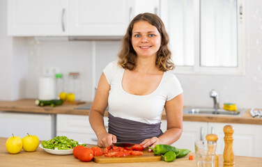Obraz na płótnie Canvas Young smiling woman chopping vegetables in home kitchen, preparing vegan dish