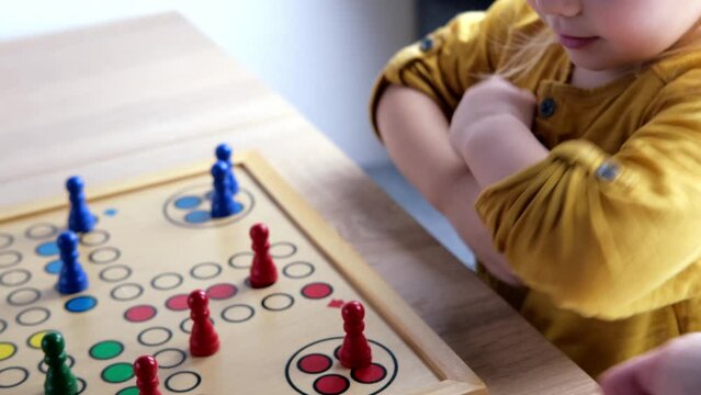 close-up of hands of small child manipulate with wooden figurines of family board game, smart kid, 2-year-old girl is learning to count, Cross and circle game Parcheesi, foreground focus