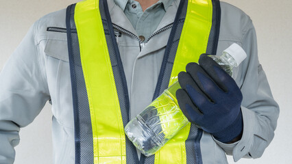 プラスチックボトルを持つ作業服の男性｜建設業の熱中症対策イメージ