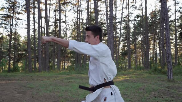 One man karateka caucasian male training karate strikes in the forest in woods in nature in day or evening wear kimono and black belt real people martial arts concept