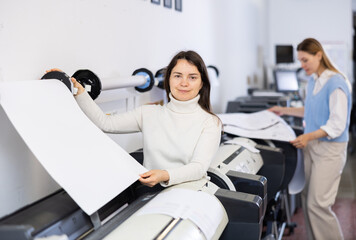 Female print worker controlling printing process on modern offset machine in print shop