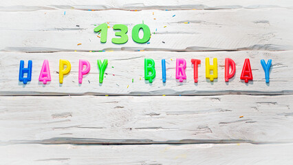 Top view of happy birthday candle numbers copy space on wooden white pastel boards. Beautiful birthday card with number 130 - obrazy, fototapety, plakaty