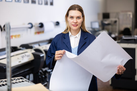 Portrait of positive woman printing office worker with large format piece of paper.