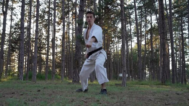 Man training karate in the forest one male athlete karateka caucasian practitioner doing kata in nature in the woods in day real people