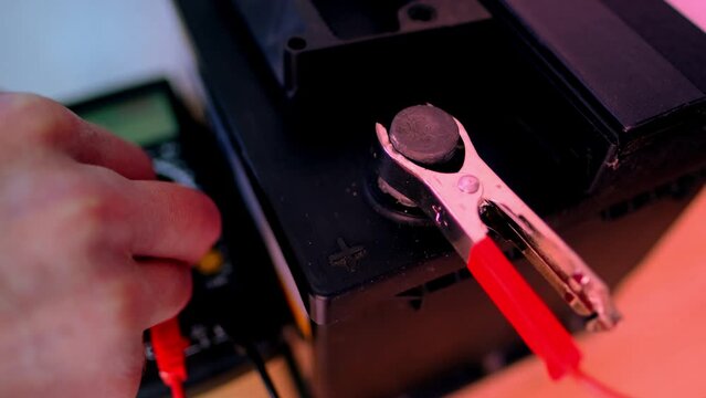 close-up car battery, red terminals are attached to the wires from the charger, the male hand checks the charge level, the concept of checking the battery charge with an electronic multimeter