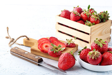 Fresh strawberries in a wooden box and strawberry slices on a cutting board with a knife.