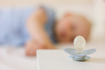 Obraz na płótnie Canvas Little baby boy is peacefully sleeping and a pacifier dummy liying on table near bed.