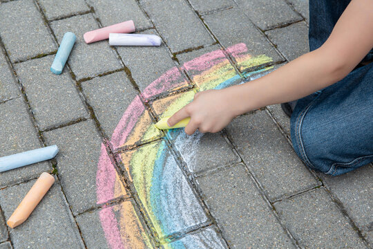 A child drawing a rainbow on the street with colored chalk. Selective focus. Kid. A child is playing outside
