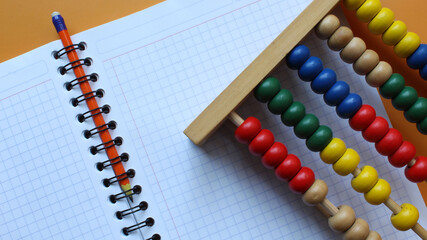 Cuaderno de cuadros con lápiz naranja y Abaco de madera con cuentas de colores.