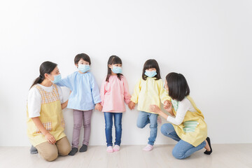 マスクを付けて幼稚園で遊ぶ子どもたちの先生