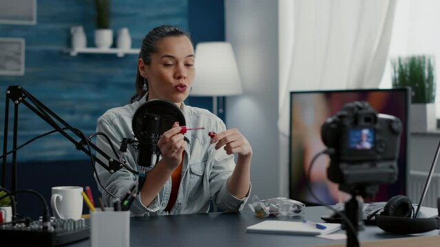 Famous content creator reviewing lipstick gloss while recording vlog for audience. Social media popular influencer doing recommendation clip for bodycare beauty cosmetics in studio.