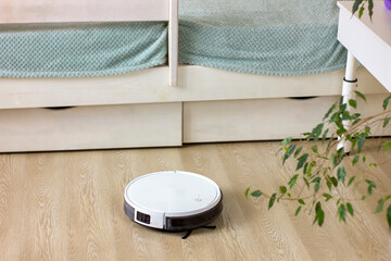 White robotic vacuum cleaner cleaning at home.