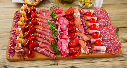 Spanish tasty meal slicing sausages fuet, ham, salami, chorizo with cherry tomatoes and olives at wooden desk, close up