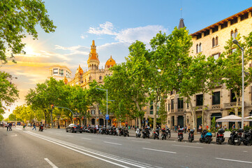 The sun sets on Paseo de Gracia avenue across from the Plaza de Catalunya in the Eixample district with the picturesque Cases Antoni Rocamora building in the sunlight in Barcelona, Spain.