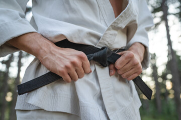 close up on hands of one man unknown karateka holding karate black belt wear white kimono gi in the forest in nature in day martial arts concept skill master