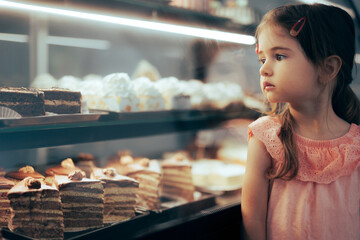 Little Girl Checking Desserts in a Showcase Window of a Confectionery Shop. Toddler child deciding...
