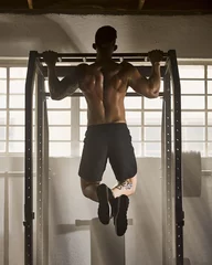 Fotobehang Strong, fitness and active man doing pull up strength and muscle full body workout with gym equipment. Rear of a fit trainer in an endurance bodybuilding or training exercise for a muscular figure © Delcio Fernandes/peopleimages.com
