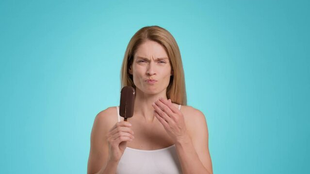 Tooth sensitivity. Middle aged woman biting ice-cream and suffering from acute toothpain, touching her painful jaw