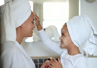 Mother and daughter bonding and spending time together on a spa day at the family home. Little girl applying face cream while smiling and having fun. Happy mom and child doing a skin facial