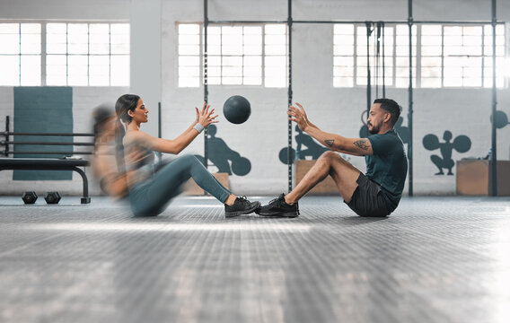 Active, sporty fitness couple or gym partners training together, doing abs exercises by throwing a weighted slam ball. Male trainer and female athlete in motion focused on workout session or class.