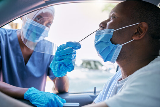 Doctor or nurse doing covid or corona virus test at a drive thru on a man sitting in a car. Medical professional taking nose swab sample from male patient through window with a PCR diagnostic kit.