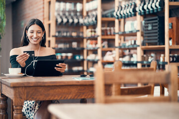 Online shopping with a credit card at a cafe by a trendy woman browsing on a tablet with earphones...