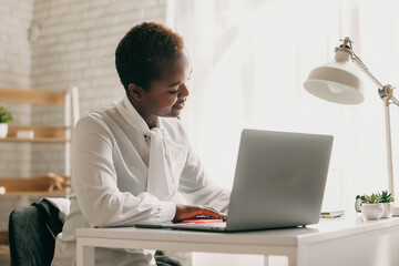 Black student, writing notes, watching webinar on laptop, studying online. Attending virtual business meeting. Seminar.