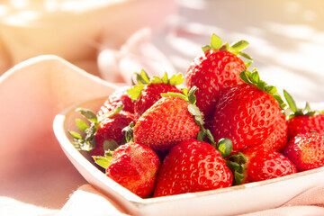 Delicious fresh red strawberries, on a rustic plate, under the summer sun