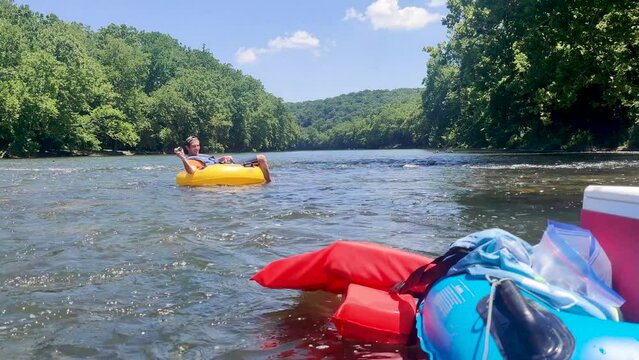 A static shot of a man inner tubing down clear creek to cool off from the summer heat