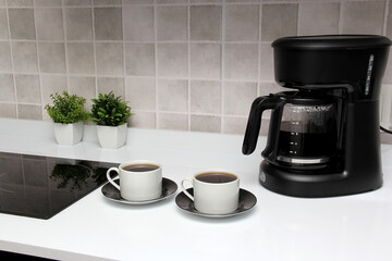 Freshly prepared coffee in a filter coffee machine served in white cups that is rich in antioxidants, fights Alzheimer's and Parkinson's, produces tachycardia and insomnia
