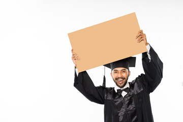 Laughing male graduate student wearing toga holding cardboard blank space on isolated background