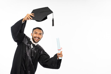Young graduate male student in toga holding up hat standing on white background